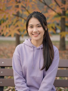 Vietnamese woman in lavender hoodie sitting on park bench in autumn